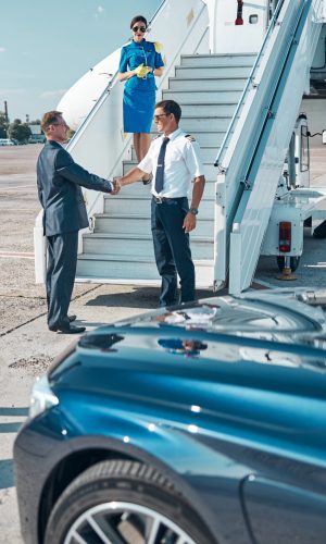 Elegant businessman coming to plane by car with driver and shaking hands with pilot before flight