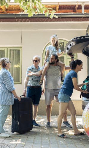 Relaxed people leaving on summer journey, putting travel bags and inflatable in automobile trunk. European family travelling together on vacation journey, loading luggage and suitcase.
