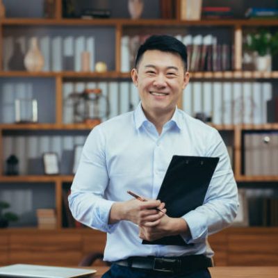 Portrait of a successful Asian teacher, a man in a shirt looking at the camera and smiling, in the classic office of the university director